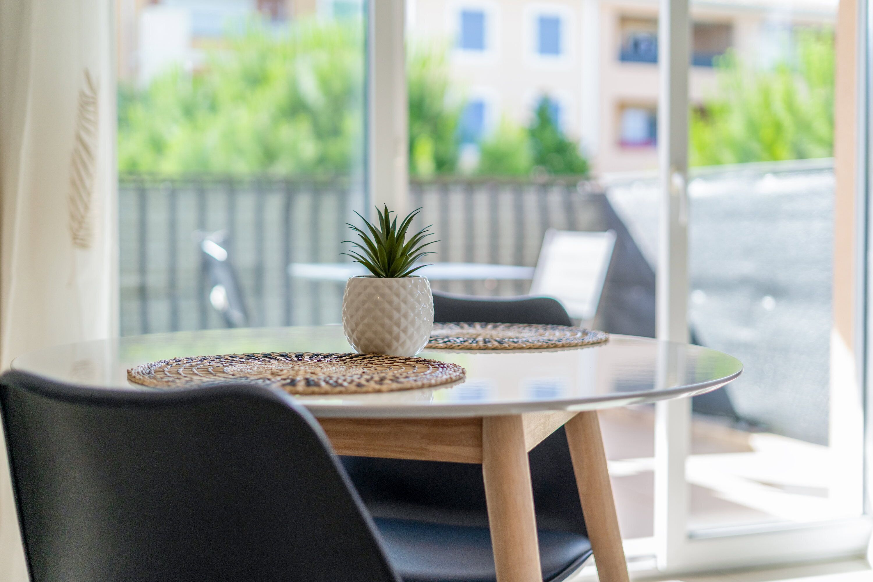 Een tafel met een bloempot, twee gevlochten placemats en zwarte stoelen.