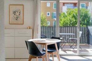 Ein moderner Essbereich mit einem runden Tisch, zwei Stühlen und Blick auf einen Balkon mit Geländer und Grünpflanzen.