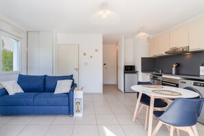 Ein modernes Apartment mit einem blauen Sofa, einem Esstisch mit Stühlen, einer Küchenzeile und einem großen Fenster.