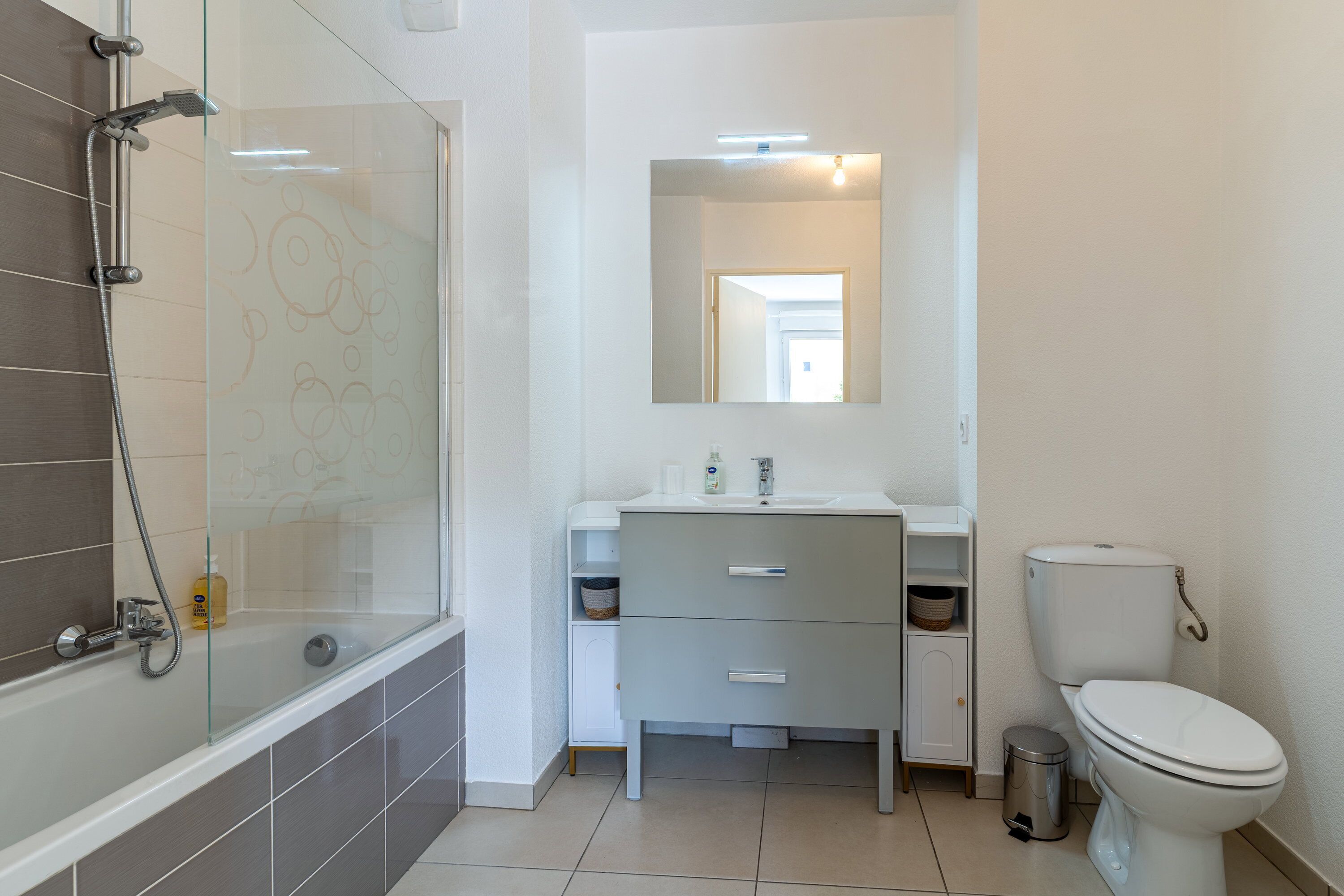 A modern bathroom with a glass shower enclosure, a white sink with a mirror above, and a toilet.