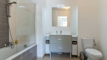 A modern bathroom with a glass shower enclosure, a white sink with a mirror above, and a toilet.