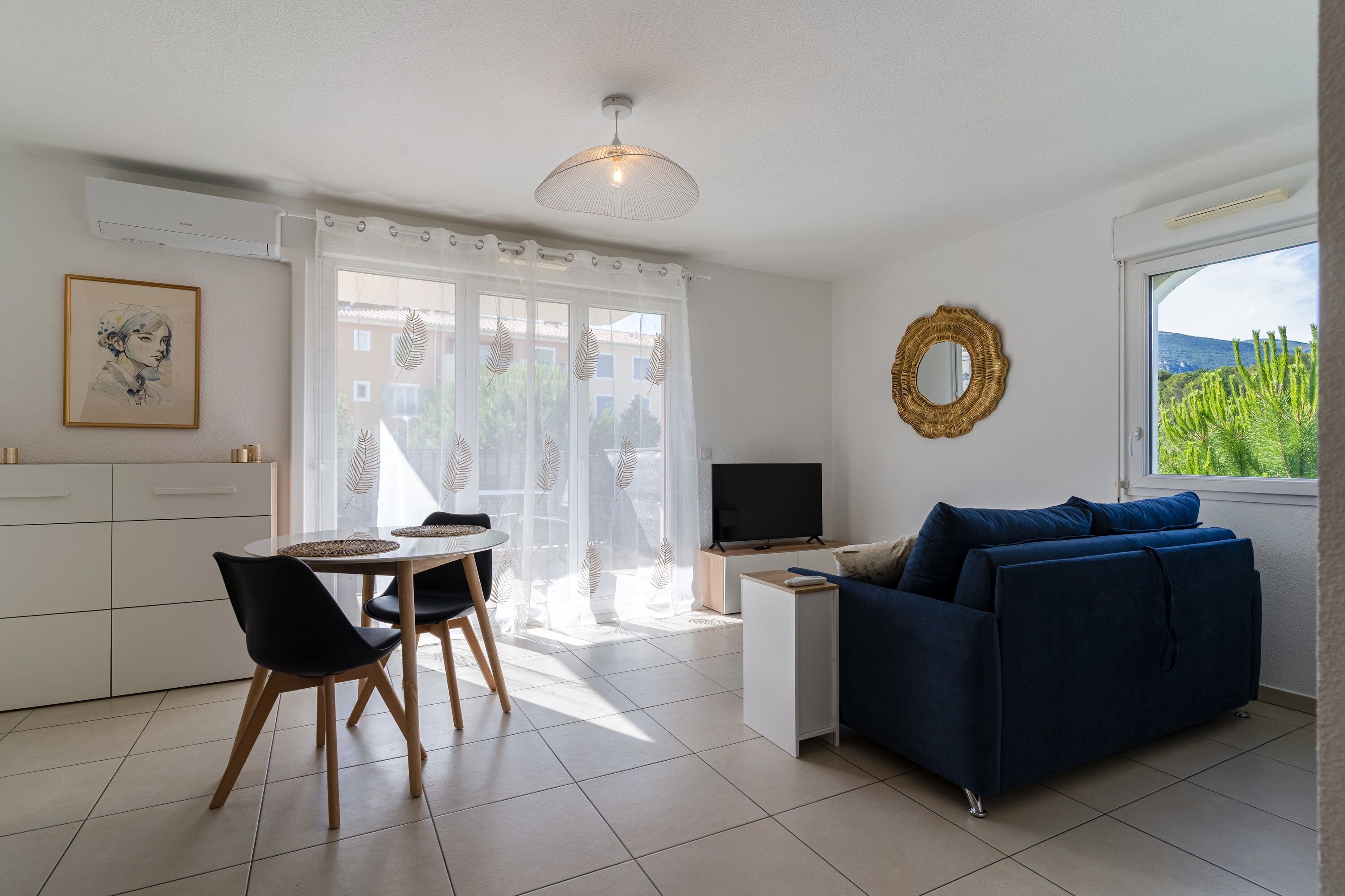 Een moderne woonkamer met een blauwe bank, een televisie en een eethoek met een tafel en stoelen.