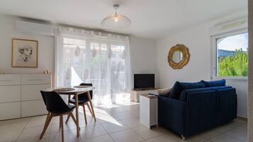 Een moderne woonkamer met een blauwe bank, een televisie en een eethoek met een tafel en stoelen.