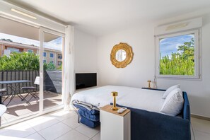 Ein Schlafzimmer mit Bett, Fernseher, Nachttisch mit Lampe, Fenster mit Aussicht und einer Glastür zu einem Außenbereich mit Tisch und Stühlen.