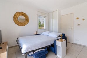 Ein Schlafzimmer mit einem Bett, Nachttischlampen, einem Fenster, einer Tür und einem an der Wand befestigten Spiegel.