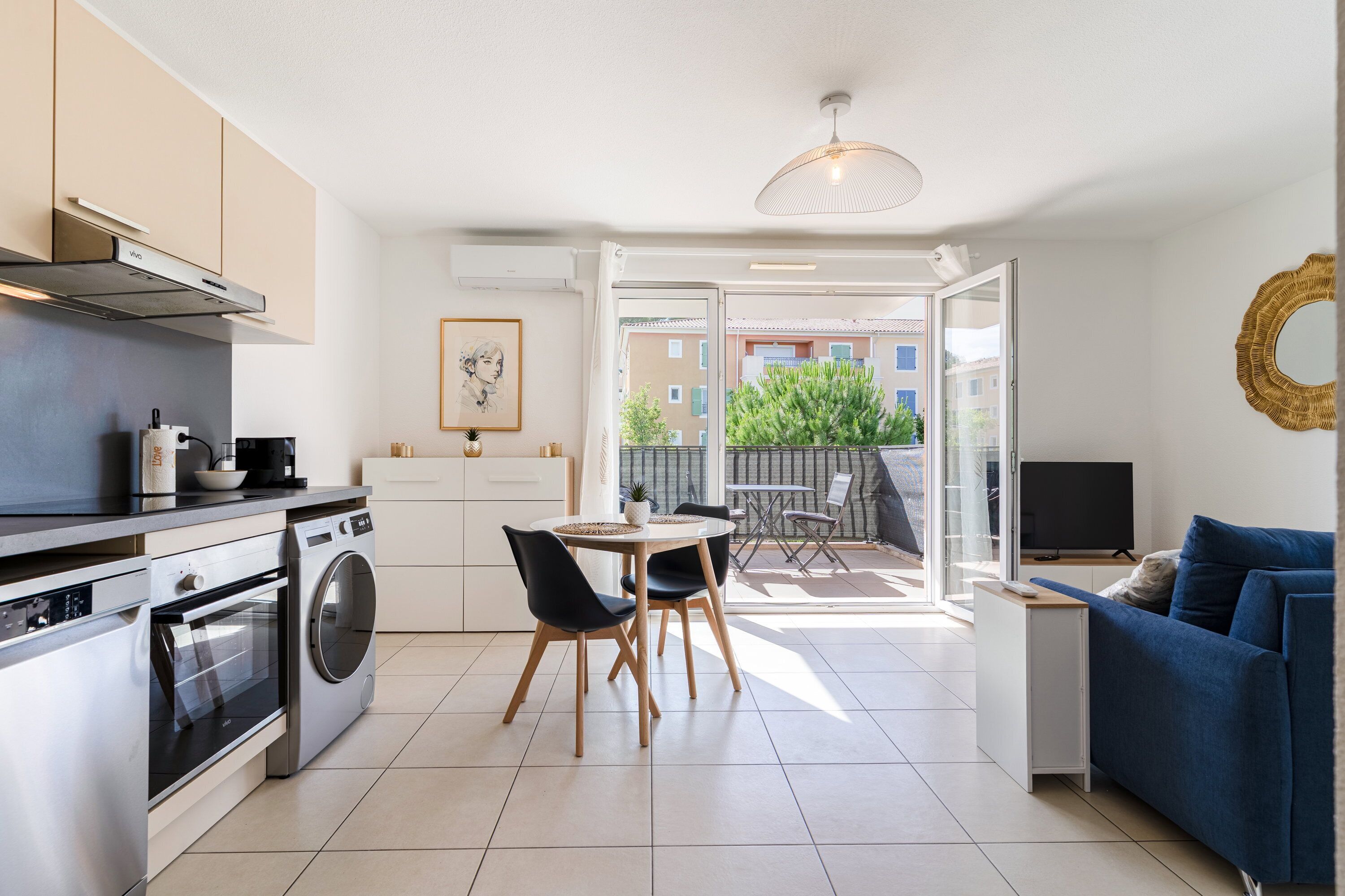 A modern kitchen with a washing machine, a dining area with a table and chairs, and a living area with a sofa and a TV.