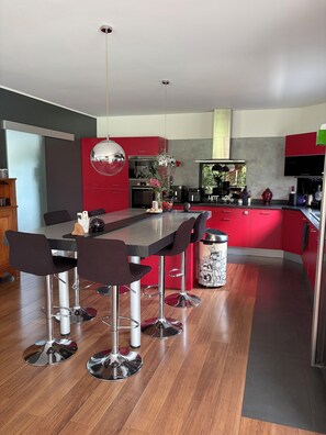 A modern kitchen with red cabinets, a central island with bar stools, stainless steel appliances, and a hanging light fixture. - A cozy villa and spa between the ocean and the Basque Country... Le Clos des Chats Heureux (Saint-Martin-de-Seignanx)