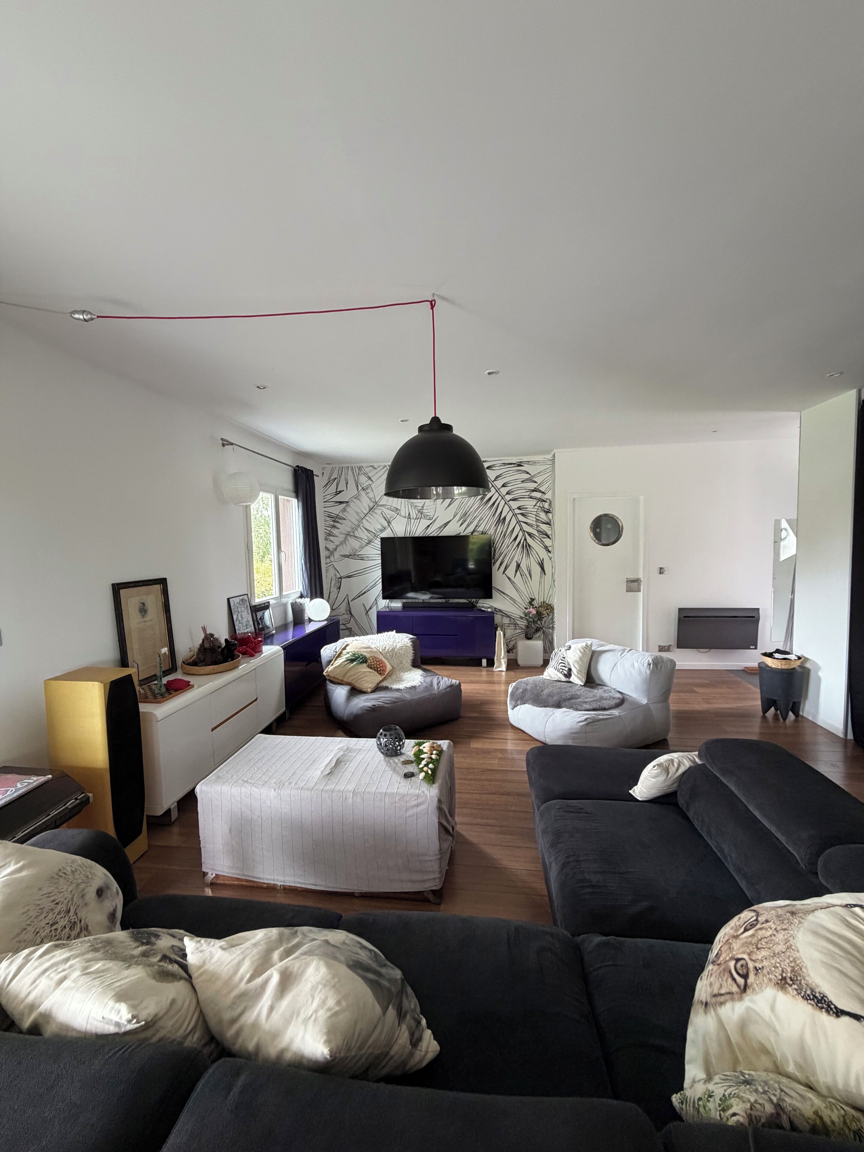 Un salon moderne avec un canapé, un pouf et un téléviseur.
