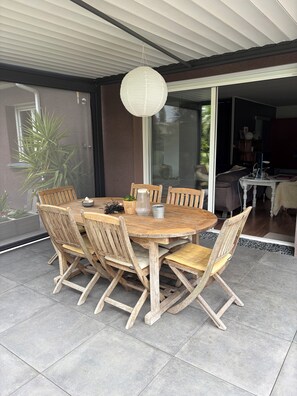 A round wooden table with six chairs, a hanging light fixture, and a glass door leading to an interior space. - A cozy villa and spa between the ocean and the Basque Country... Le Clos des Chats Heureux (Saint-Martin-de-Seignanx)