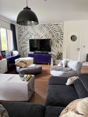 A modern living room with a flat-screen TV, a large black pendant light, and a wall with a leaf pattern. - A cozy villa and spa between the ocean and the Basque Country... Le Clos des Chats Heureux (Saint-Martin-de-Seignanx)