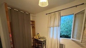 Une chambre à coucher avec un lit, un bureau avec une chaise, un luminaire suspendu et une fenêtre avec des rideaux.