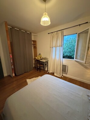 Ein Schlafzimmer mit Bett, Schreibtisch und Stuhl, einer Pendelleuchte sowie einem Fenster mit Vorhängen.