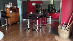 Une cuisine moderne avec des meubles rouges, un coin repas doté de tabourets de bar et un meuble en bois surmonté d’un vase blanc.