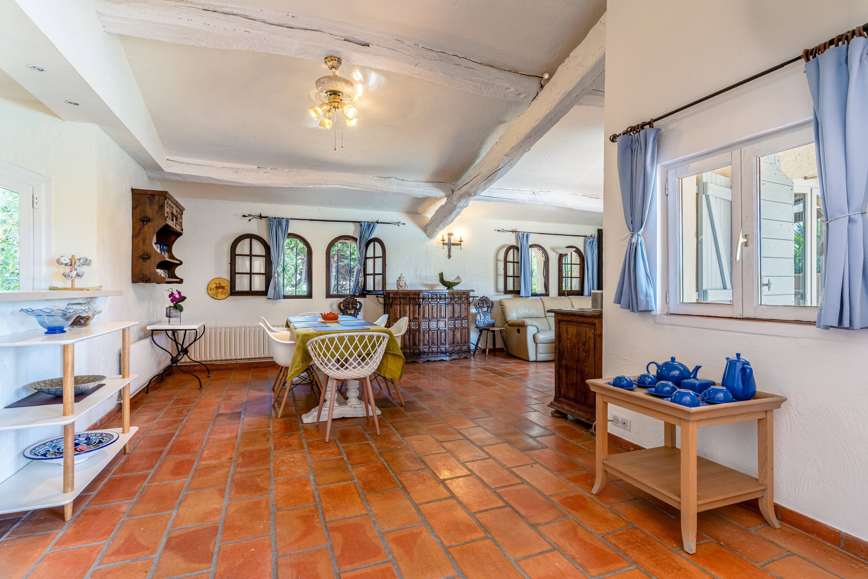 A spacious living area with a dining table, chairs, a sofa, and a kitchen area with a stove and cabinets.