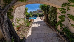 Un vialetto in pietra conduce a una zona piscina, circondata dal verde e da un cielo azzurro intenso.