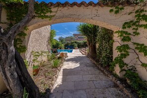 A stone pathway leading to a pool area, surrounded by greenery and a clear blue sky. - L'Absolu Azur : Bulle de Calme & Piscine (Grasse)