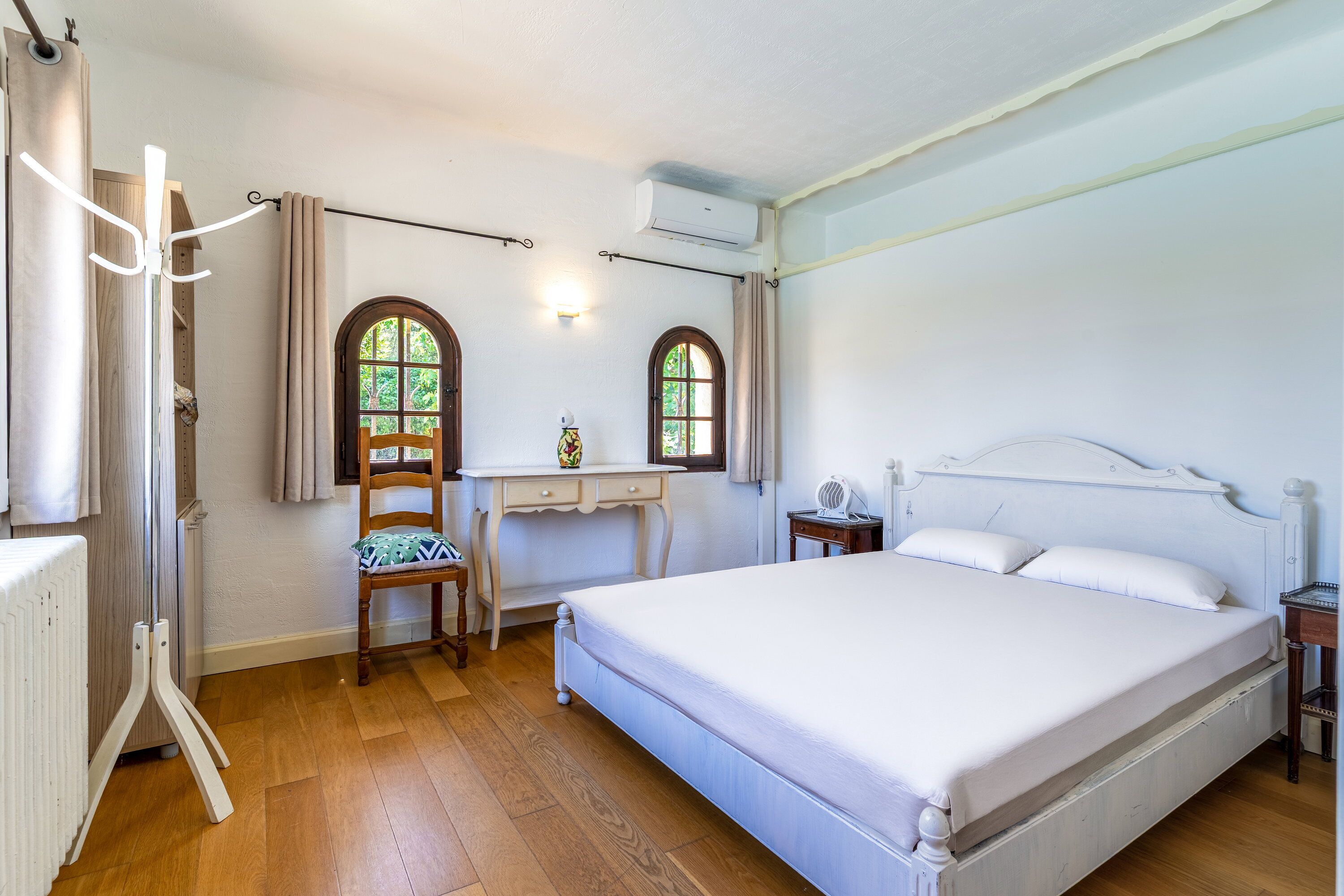 A bedroom with a bed, a desk, two windows, and a radiator.