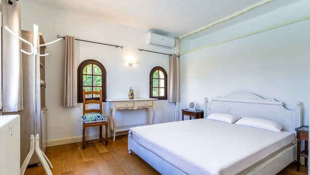 Una camera da letto con un letto, una scrivania, due finestre e un termosifone.