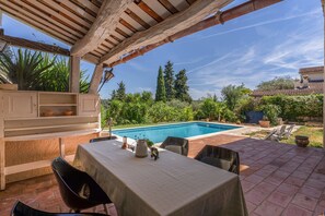 Une terrasse extérieure avec une piscine, entourée de verdure et agrémentée d’une pergola.