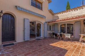 A two-story building with a patio area featuring a brick floor and outdoor furniture. - L'Absolu Azur : Douceur de vivre & piscine (Grasse)