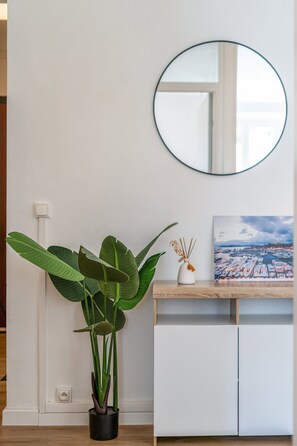 A room with a potted plant, a round mirror on the wall, a small table with a vase, and a framed picture. - Au Cœur de Cannes : Croisette & Palais à Pied (Cannes)
