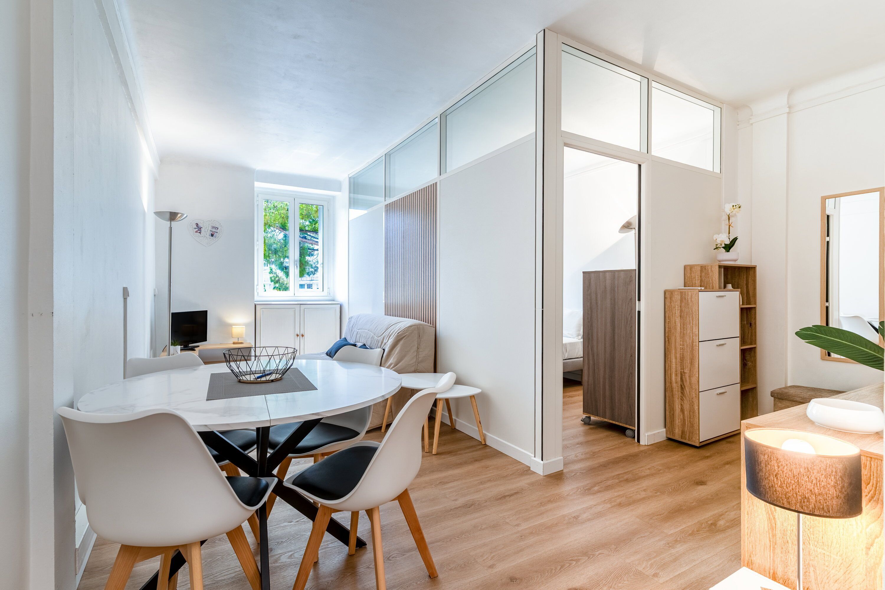 Ein modernes Wohnzimmer mit Esstisch, Stühlen und einer Couch. Ein Fernseher, eine Lampe und eine Pflanze sind ebenfalls vorhanden.
