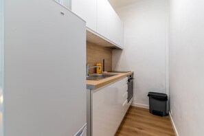 Eine kleine Küche mit weißen Schränken, einer Holz Arbeitsplatte, einer Edelstahl-Spüle und einem schwarzen Mülleimer.
