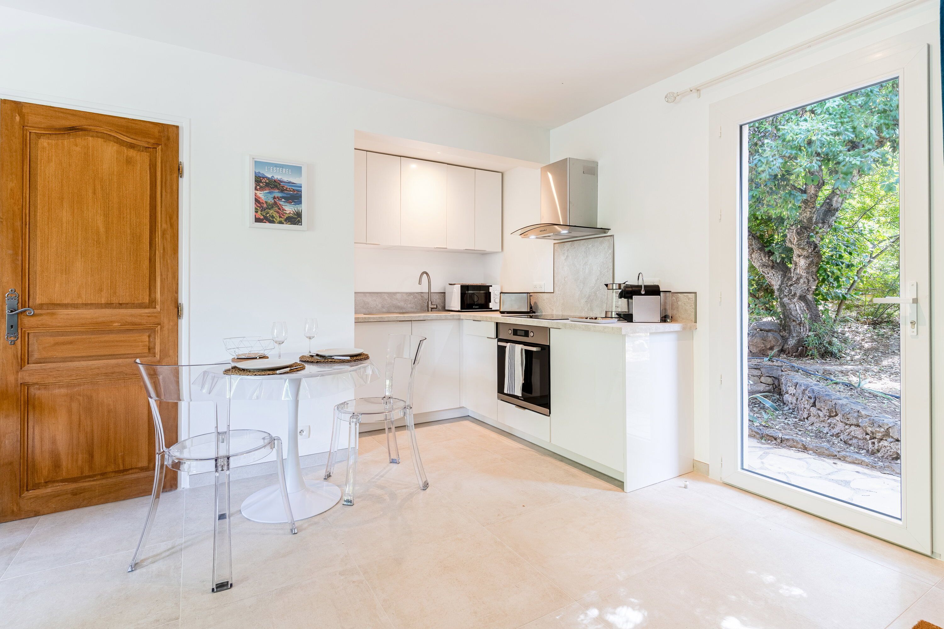 A modern kitchen with a dining area, featuring a wooden door, a view of greenery, and a small oven.
