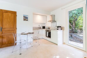 A modern kitchen with a dining area, featuring a wooden door, a view of greenery, and a small oven. - La Villa Estérelle — Vue golf, piscine & élégance (Saint Raphael)