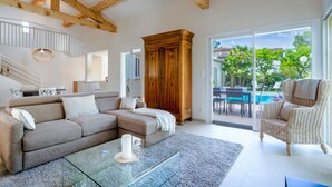 A living room with a sectional sofa, a glass coffee table, a wooden cabinet, and a wicker chair. - La Villa Estérelle — Vue golf, piscine & élégance (Saint Raphael)