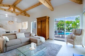 Ein Wohnzimmer mit Ecksofa, Glastisch, Holzschrank und Korbstuhl.