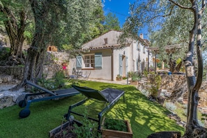 A house with a stone wall, a patio with a table and chairs, and a lawn. - L'Échappée Parfumée, Panorama d'exception et calme (Grasse)