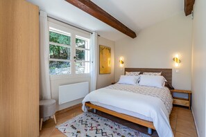 A bedroom with a bed, bedside tables, a radiator, a window with curtains, and a wall-mounted light fixture. - Douceur Parfumée — Vue Panoramique & Calme Absolu (Grasse)