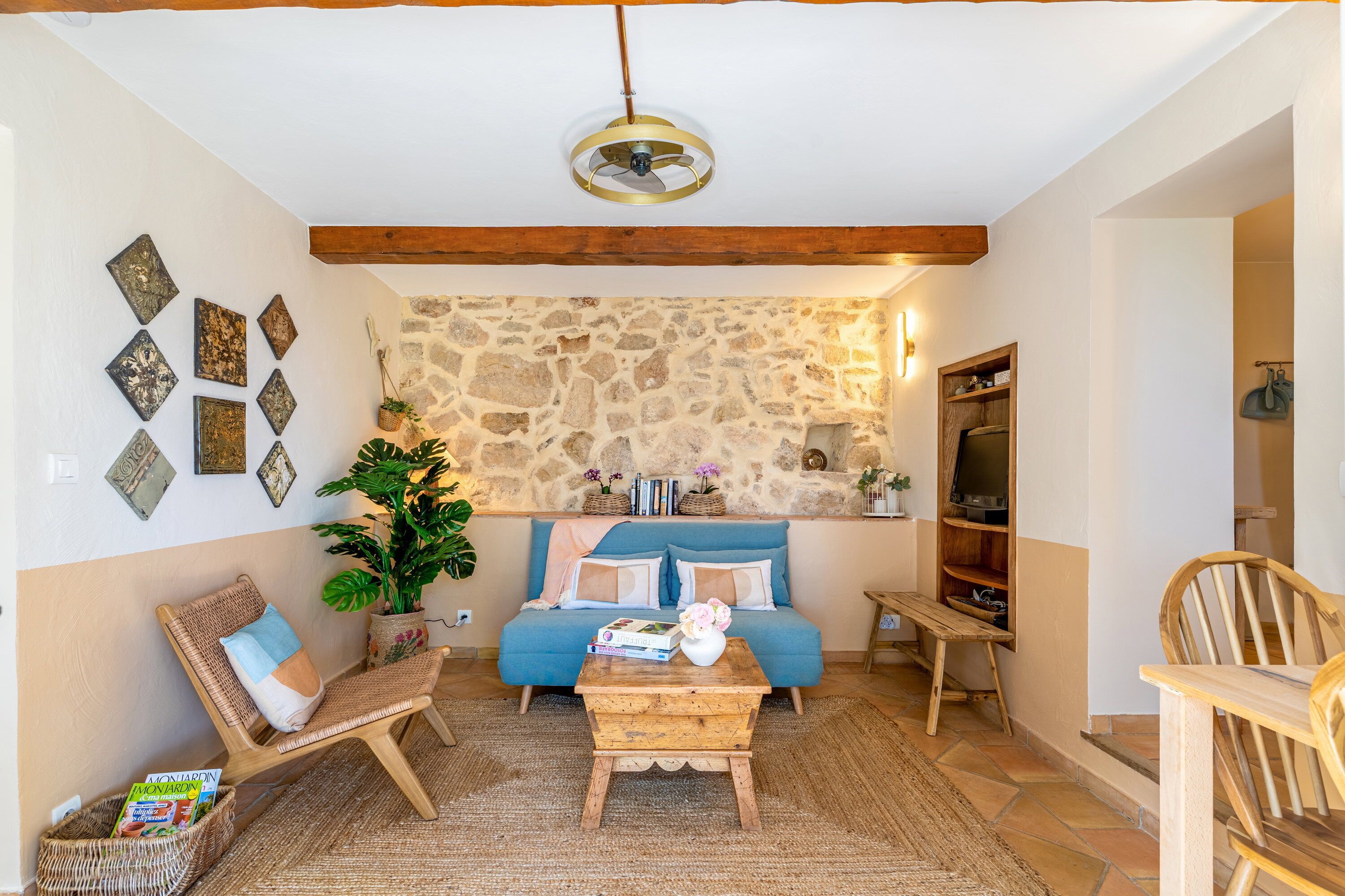 A cozy living room with a stone wall, a blue sofa, a wooden coffee table, and a wicker chair.