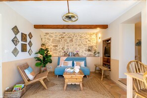 A cozy living room with a stone wall, a blue sofa, a wooden coffee table, and a wicker chair. - Douceur Parfumée — Vue Panoramique & Calme Absolu (Grasse)