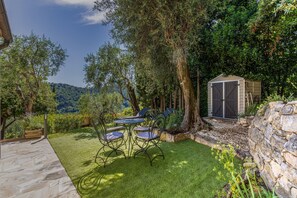 A patio with a table and chairs, surrounded by a stone wall and a small shed. - Douceur Parfumée — Vue Panoramique & Calme Absolu (Grasse)