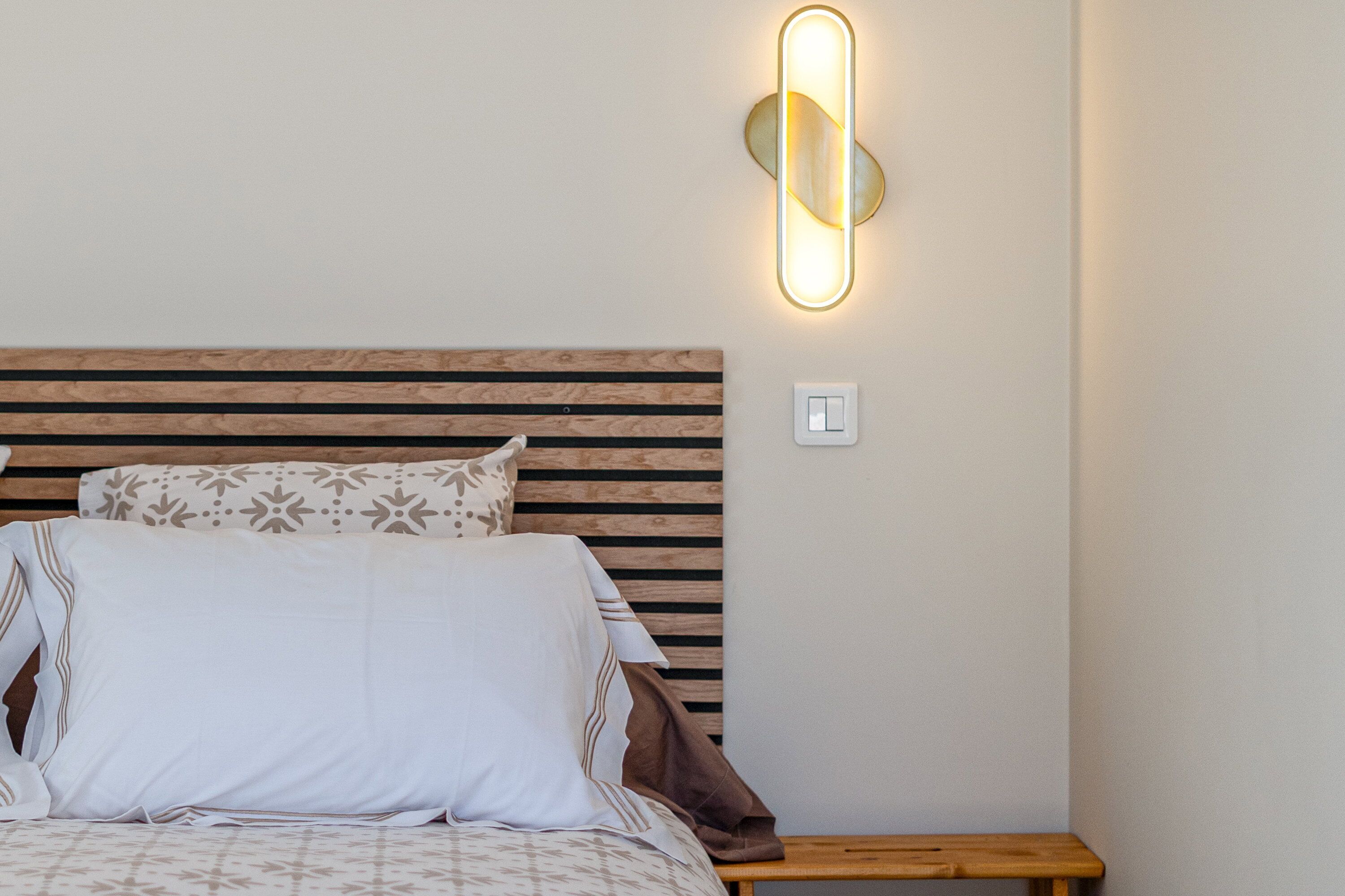 A bed with a wooden headboard, a bedside table, and a wall-mounted light fixture.