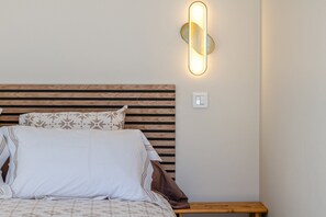 Uma cama com cabeceira de madeira, mesa de cabeceira e luminária na parede.