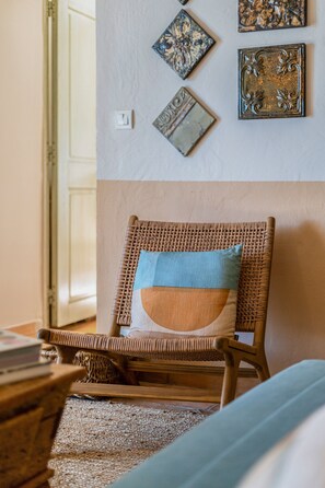 A wicker chair with a cushion, a woven rug, and wall decorations including framed pictures. - L'Échappée Parfumée, Panorama d'exception et calme (Grasse)
