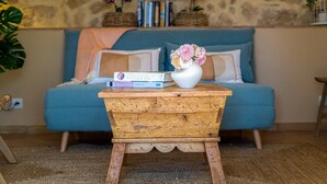 En hyggelig stue med en blå sofa, et træ sidebord med en vase blomster, og en bogreol i baggrunden.