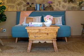 A cozy living room with a blue sofa, a wooden side table with a vase of flowers, and a bookshelf in the background. - L'Échappée Parfumée, Panorama d'exception et calme (Grasse)