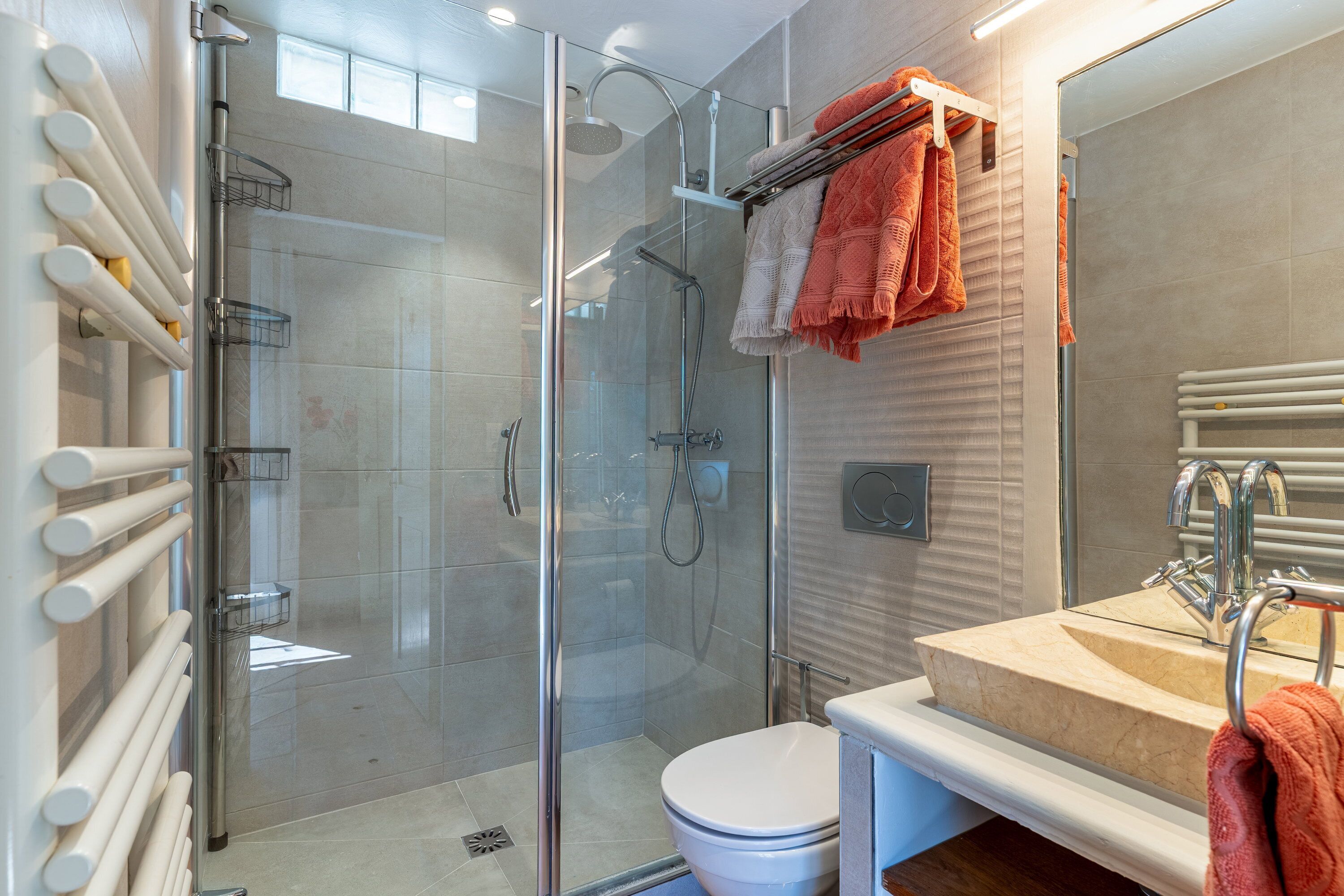 Une salle de bain moderne avec une douche à parois de verre, des toilettes blanches et un lavabo beige doté d’un porte-serviettes.
