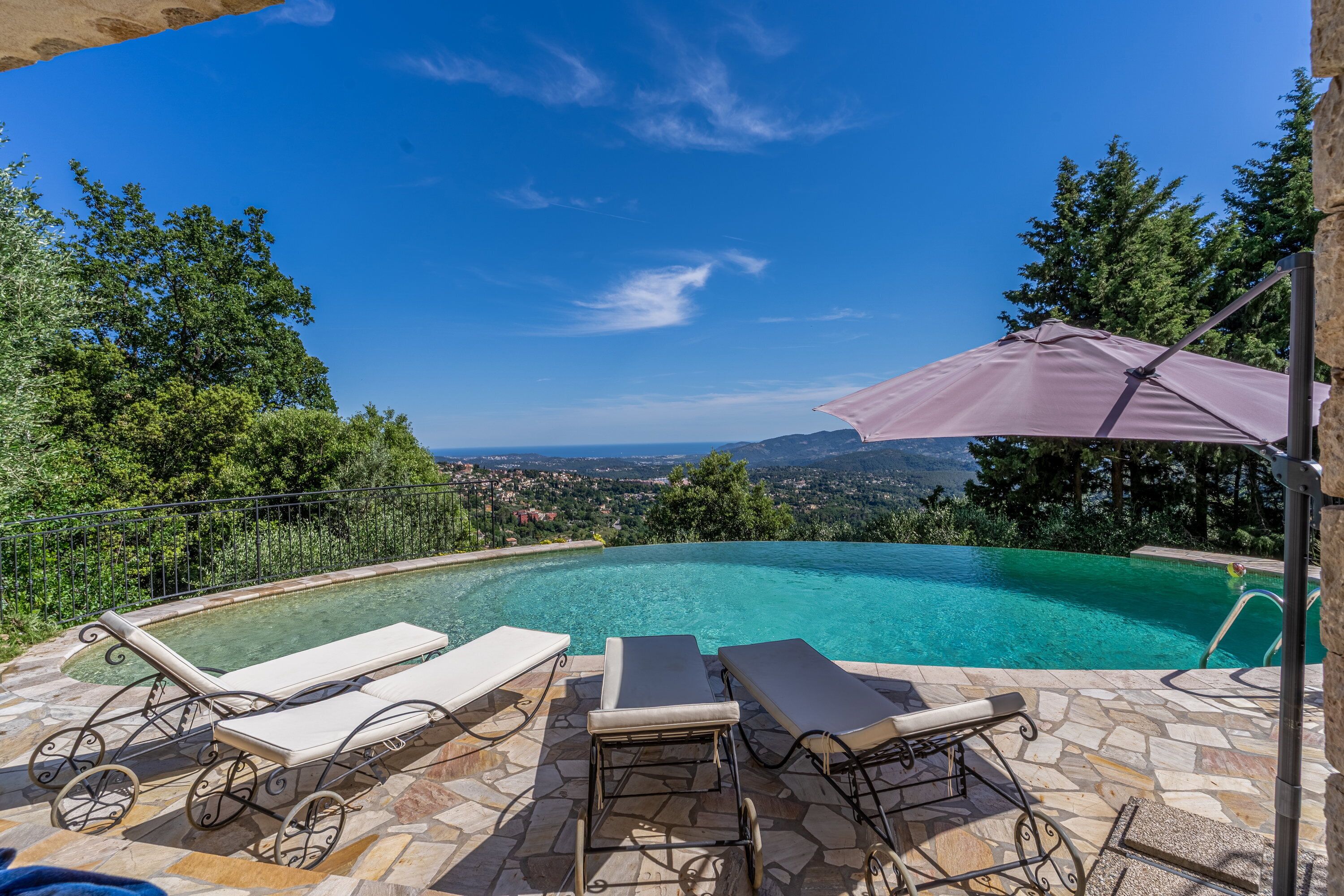 A swimming pool with lounge chairs and an umbrella, surrounded by trees and a view of the landscape.