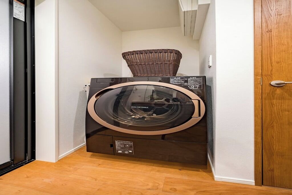 A compact, modern laundry room with a built-in washer and dryer, a wicker basket on top of the dryer, and a wooden floor.