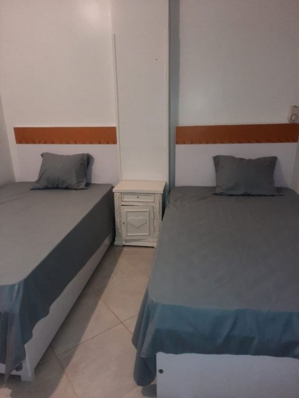 Een kamer met twee éénpersoonsbedden, elk met een kussen en een nachtkastje.