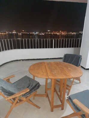 Ein Balkon mit Holztisch und -stühlen, einem Geländer und Blick auf die Stadt bei Nacht.