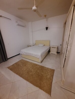 Une chambre à coucher comprenant un lit, une table de chevet, une armoire et un ventilateur de plafond.