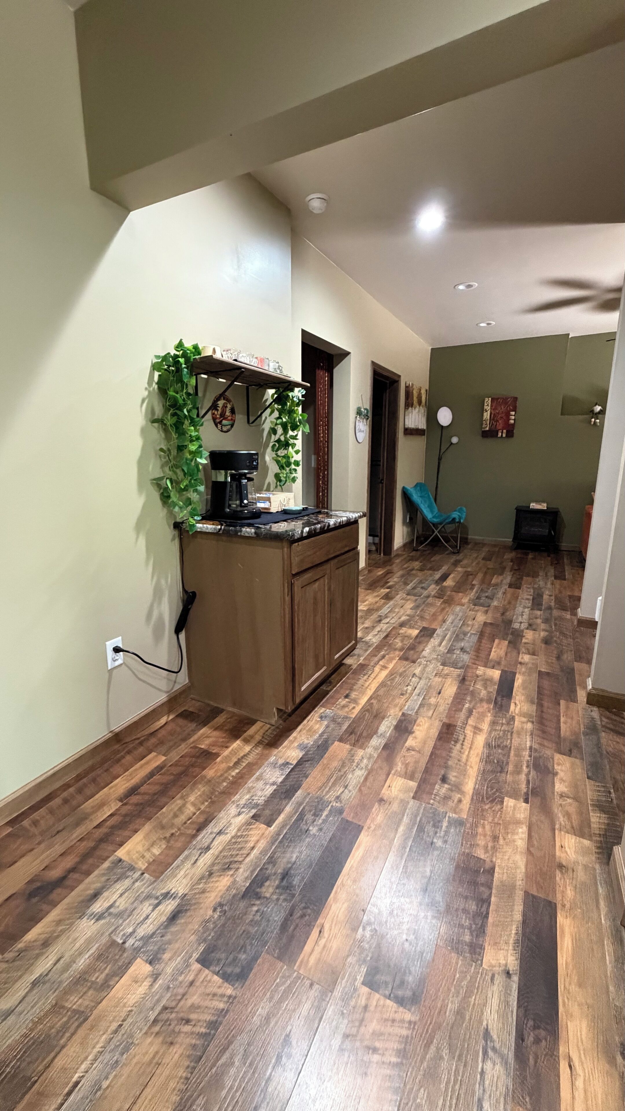 Een ruime keuken met een houten visgraatvloer, een inbouw kookeiland met een koffieapparaat, en een hangende plant.