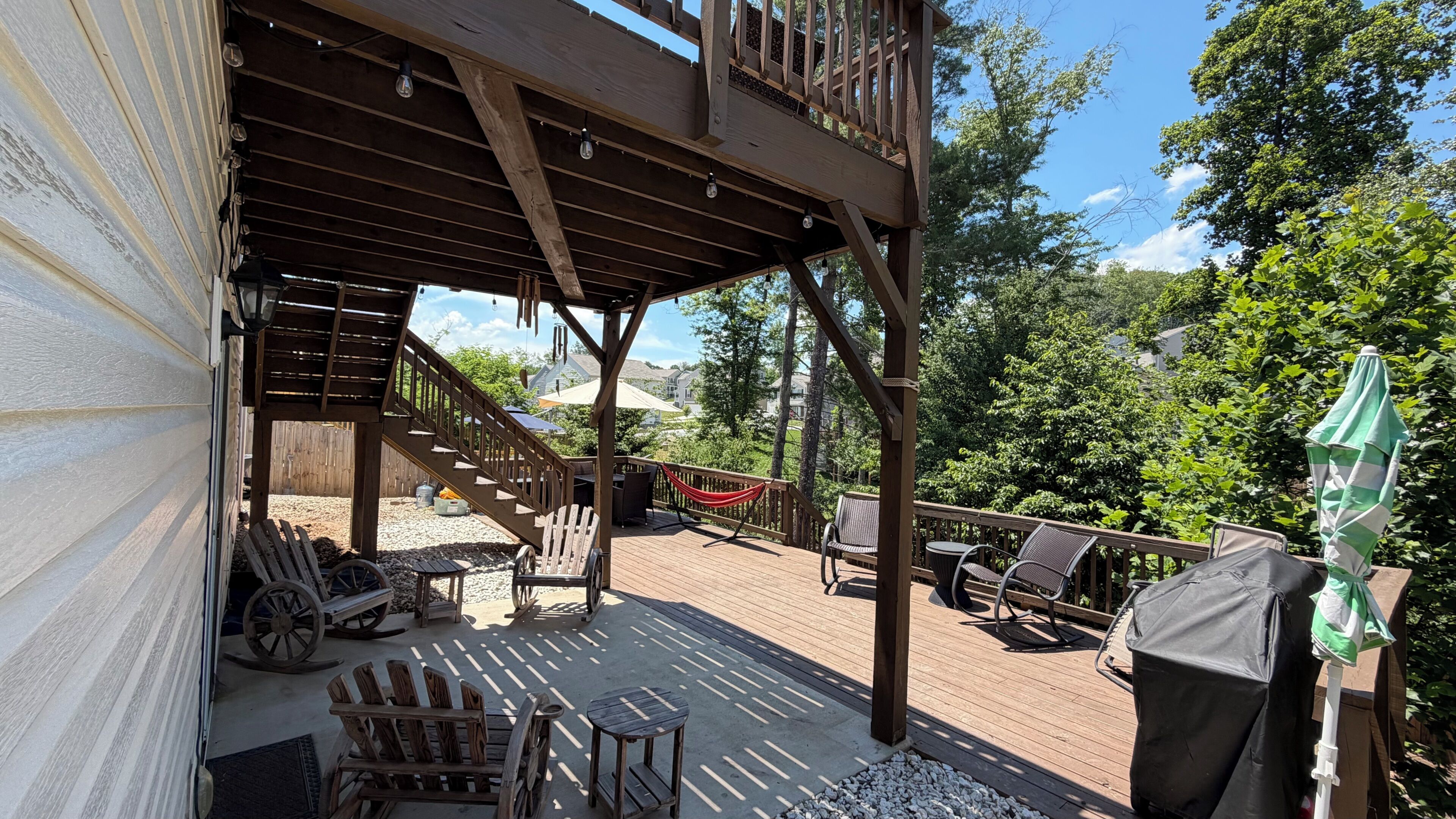 A wooden deck with outdoor furniture, a hammock, and a covered area with stairs leading to a higher level.