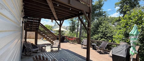 Una terraza de madera con mobiliario exterior, una hamaca y un área cubierta con escaleras que conducen a un nivel superior.